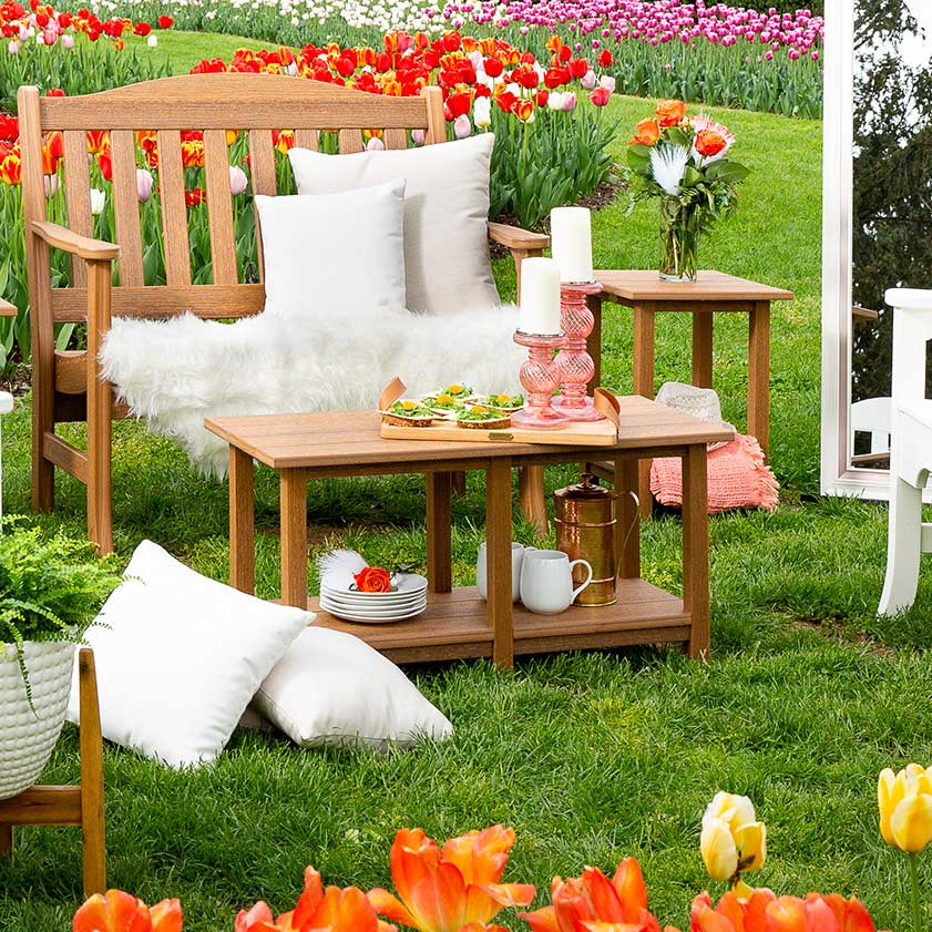 Teak poly garden coffee table and side table styled with dishes and flowers among spring tulips