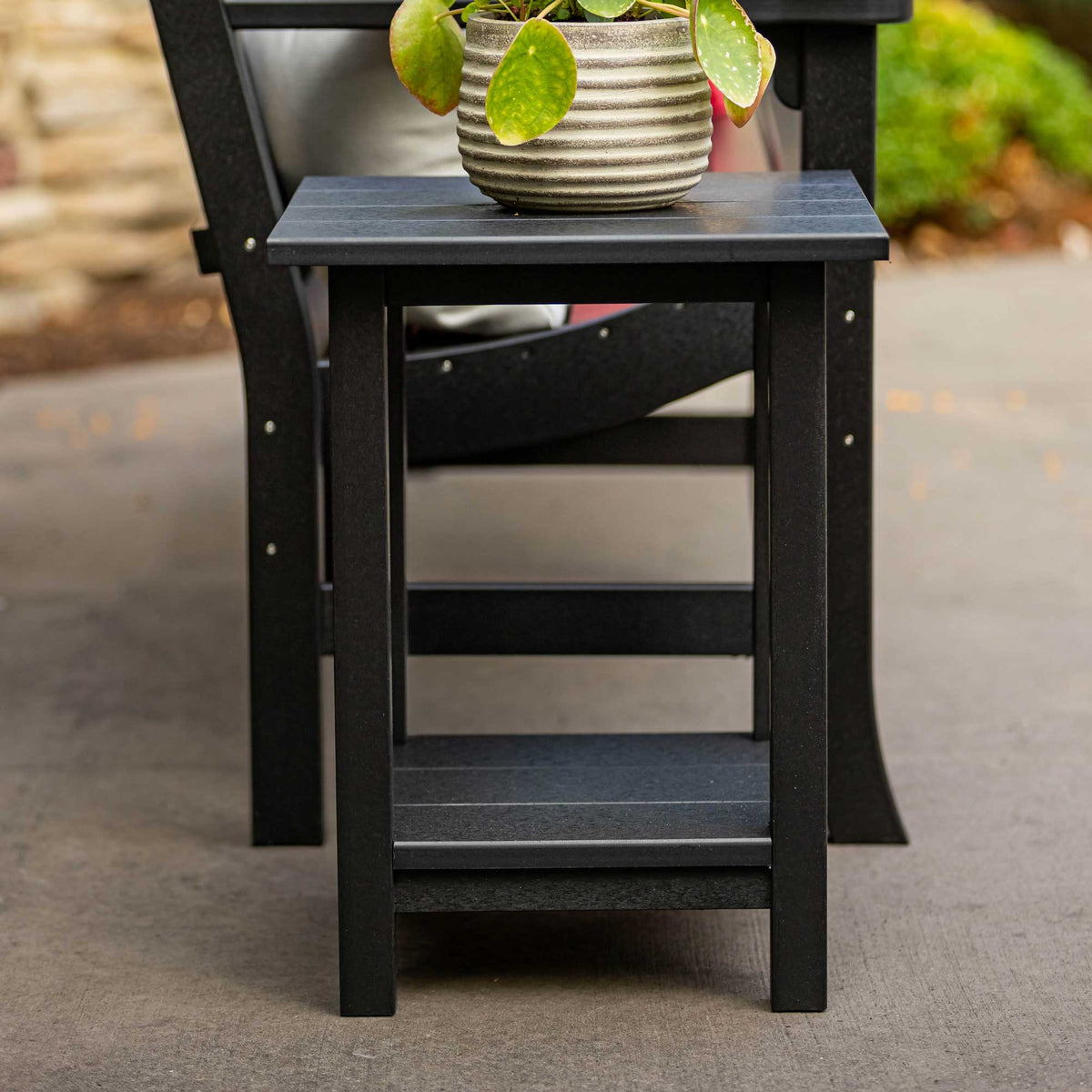Black poly end table with a slatted lower shelf beside an outdoor chair on a concrete patio