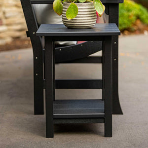 Black poly end table with a slatted lower shelf beside an outdoor chair on a concrete patio