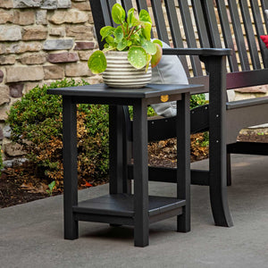 Black poly patio end table with a lower shelf, topped with a potted plant beside a garden bench