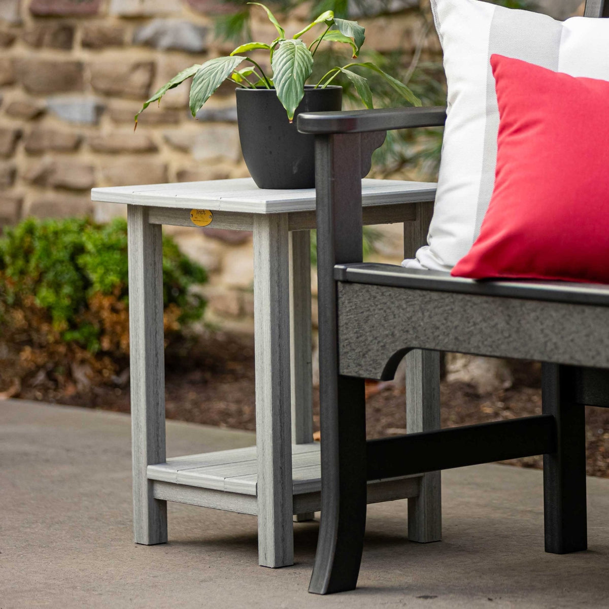 Weathered white poly side table with a plant on top and slat shelf below, next to a black bench