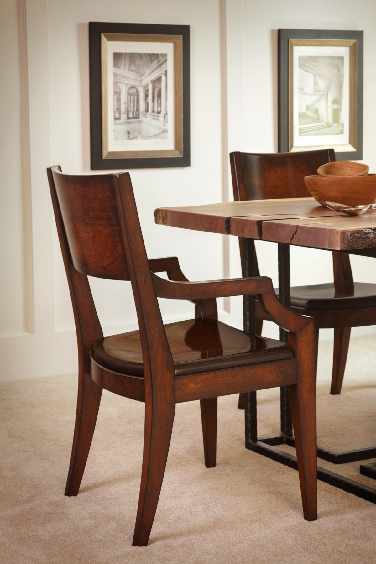 Cherry dining arm chair with a curved panel back and shaped arms pulled up to a live edge dining table
