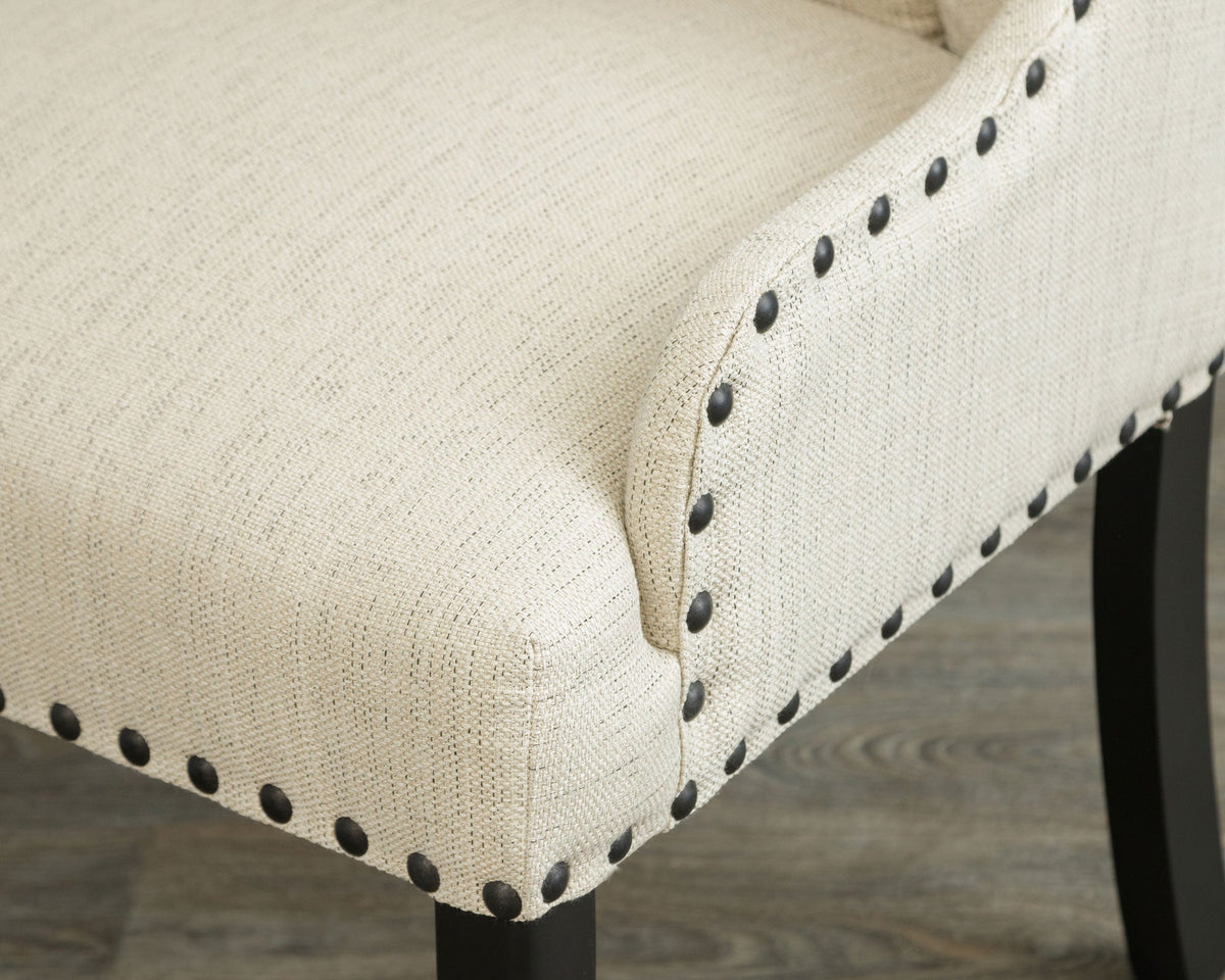 Detail of a cream upholstered chair seat and arm with black nailhead trim and a dark tapered leg