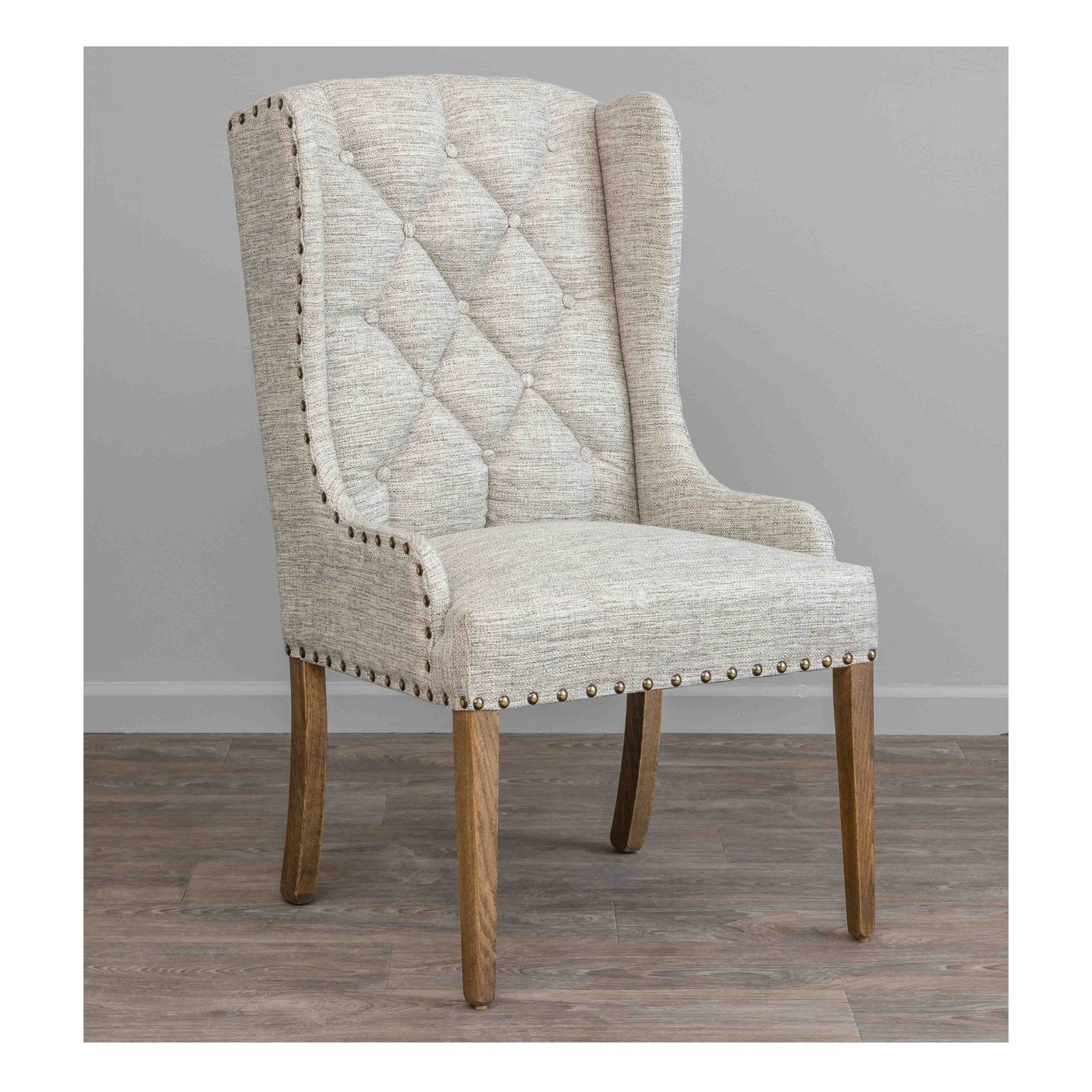 Cream tufted wing back dining arm chair with bronze nailhead trim and weathered oak tapered legs