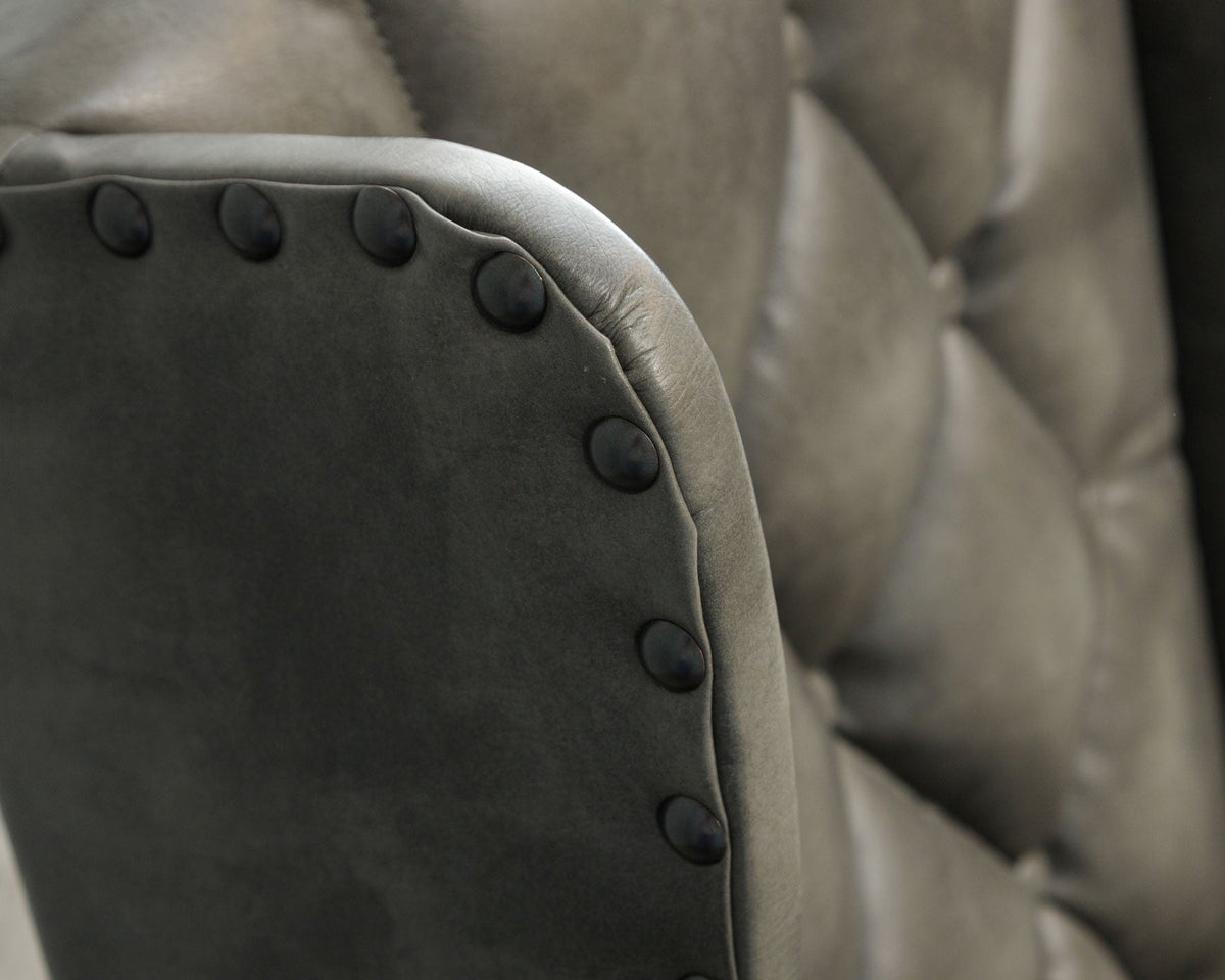 Detail of the wingback chair's dark charcoal leather wing edged with matte black nailheads against the tufted back