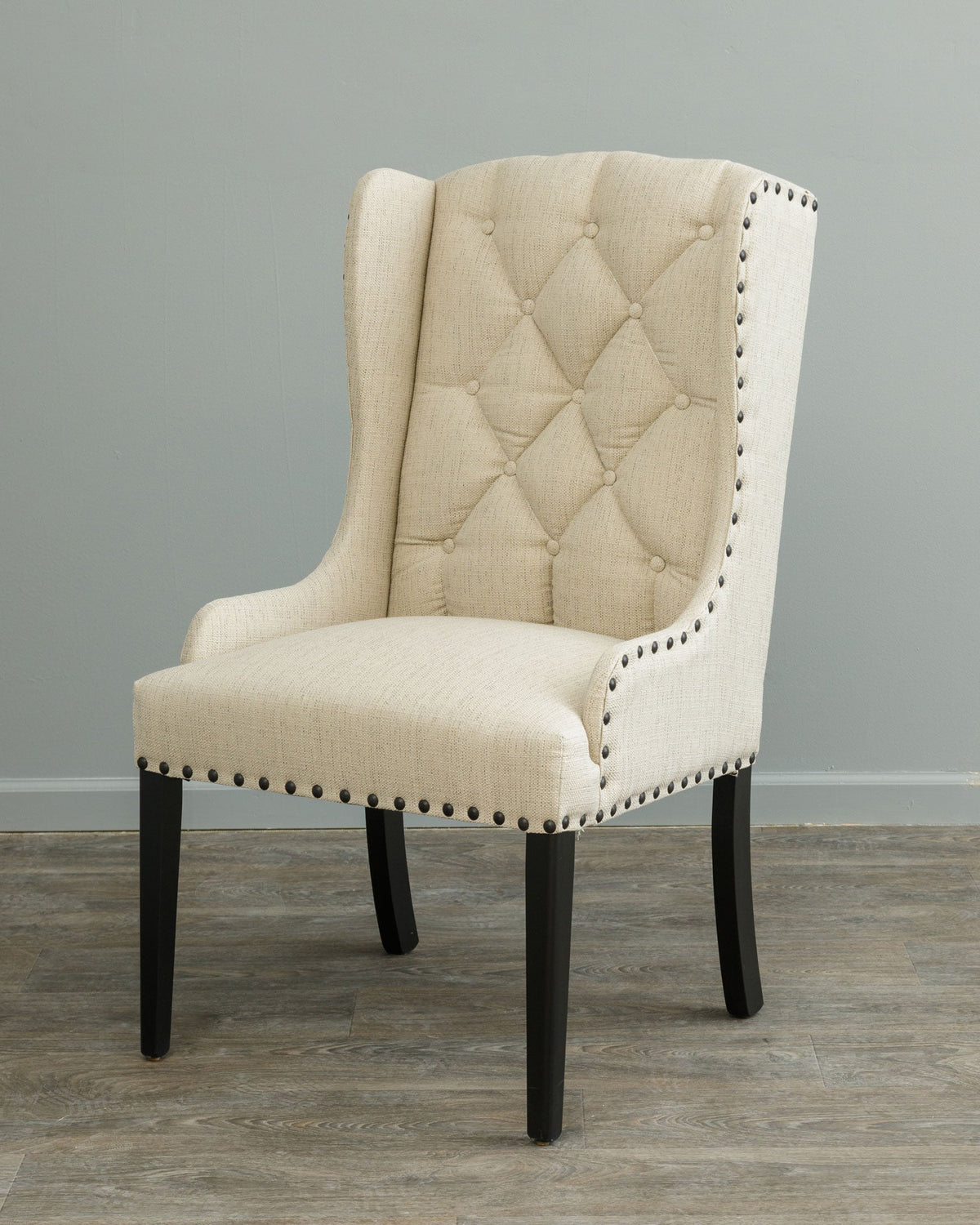 Cream linen wingback dining chair with tufted back, nailhead accents and black tapered hardwood legs