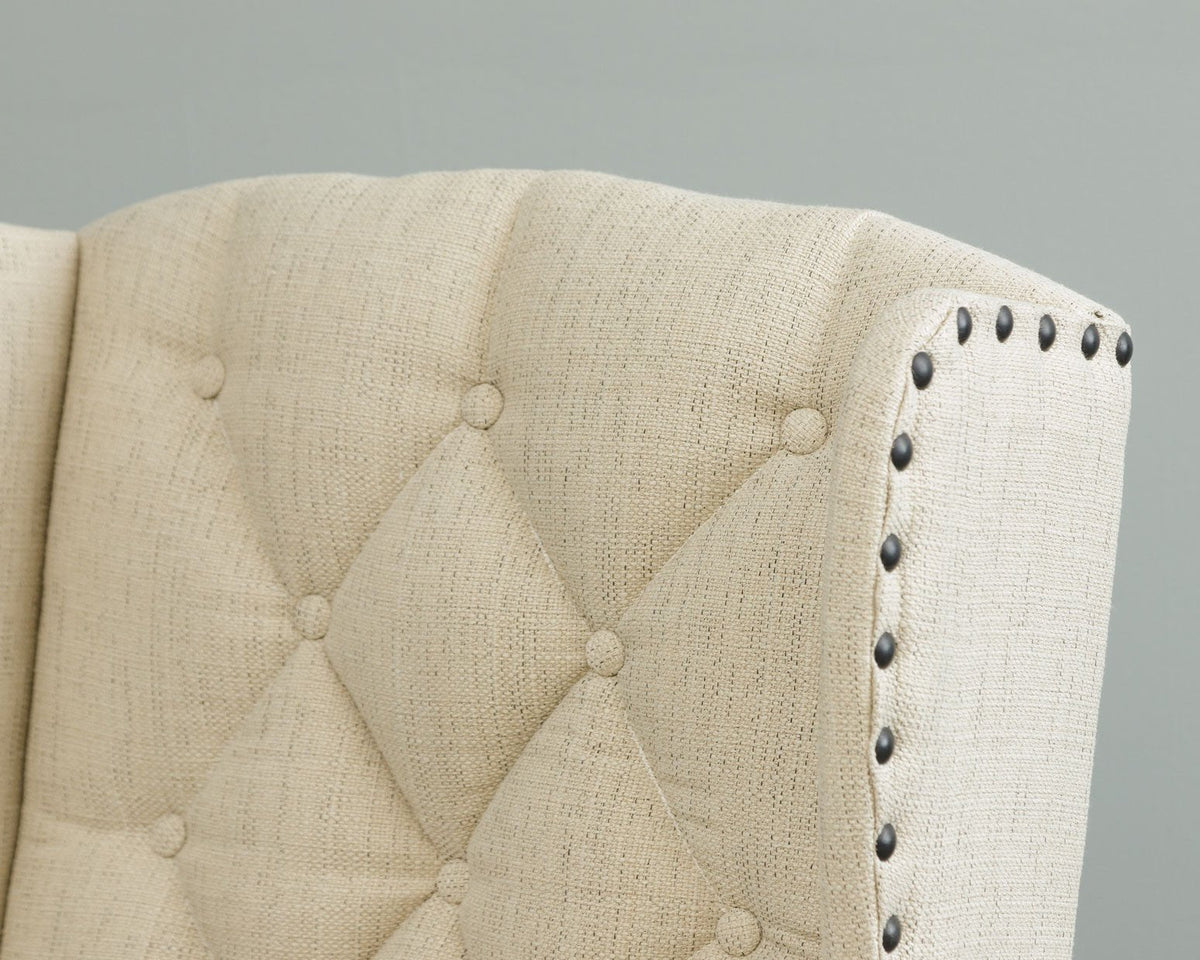 Close-up of the chair's diamond button tufting and dark bronze nailhead trim along the cream linen wing