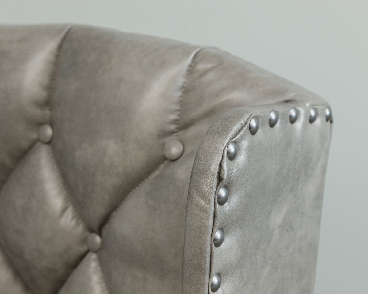 Close-up of the gray tufted leather chair back corner showing button tufting and silver nailhead trim