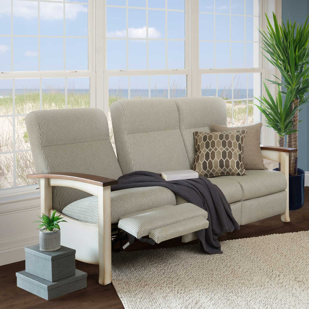 Cream framed reclining sofa in beige fabric with one footrest extended, in a sunroom overlooking the beach