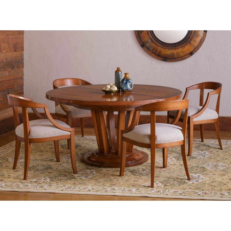 Round cherry pedestal dining table set with four curved back chairs and cream seats in a rustic dining room