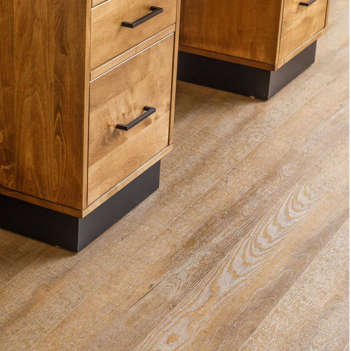 Detail of the desk pedestal bottoms with black recessed plinth bases on wide plank vinyl flooring