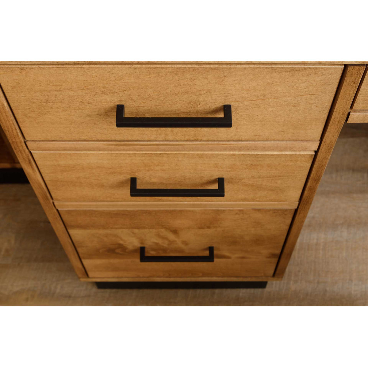 Close view of three stacked drawer fronts in golden birch with squared black bar pulls and a black base plinth