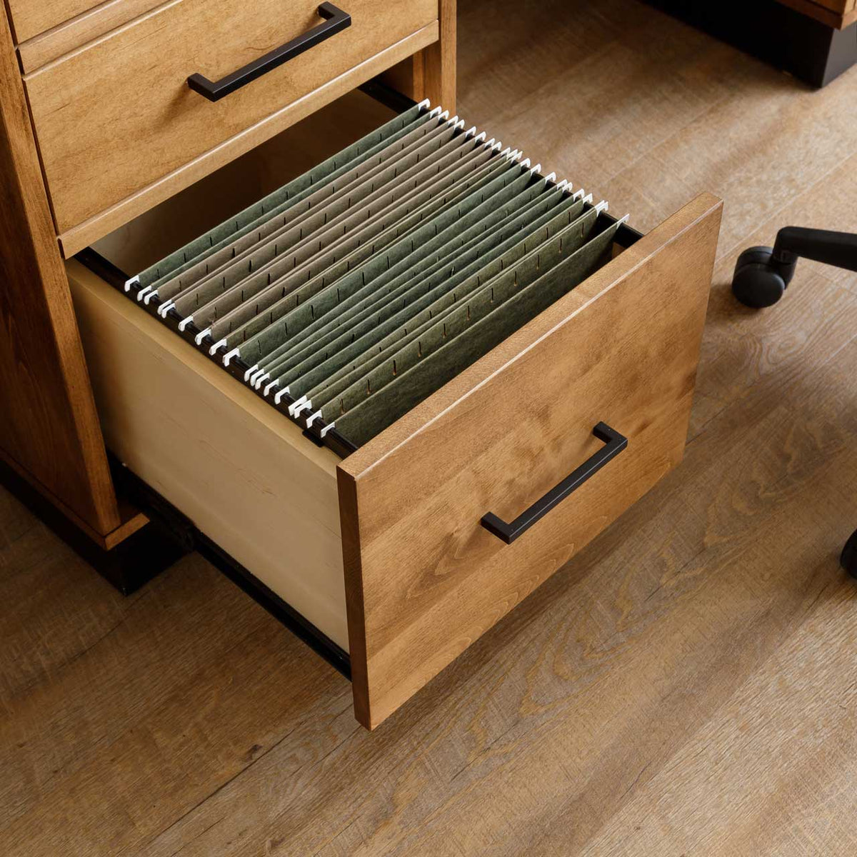 Deep file drawer open on a modern wood desk pedestal, filled with green hanging folders on smooth glides