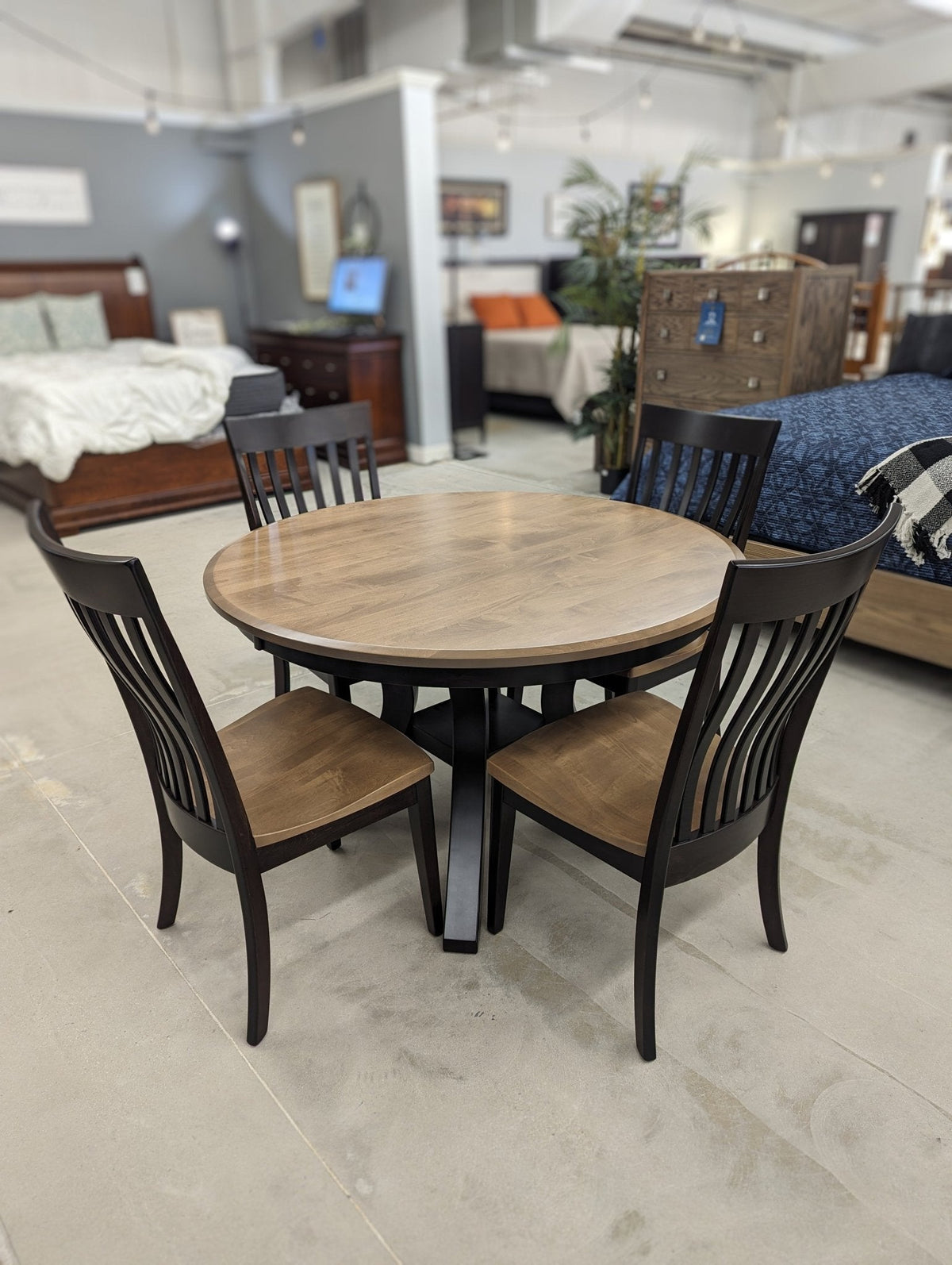 Two-tone round dining table with a natural wood top and black pedestal base, plus four black slat back chairs