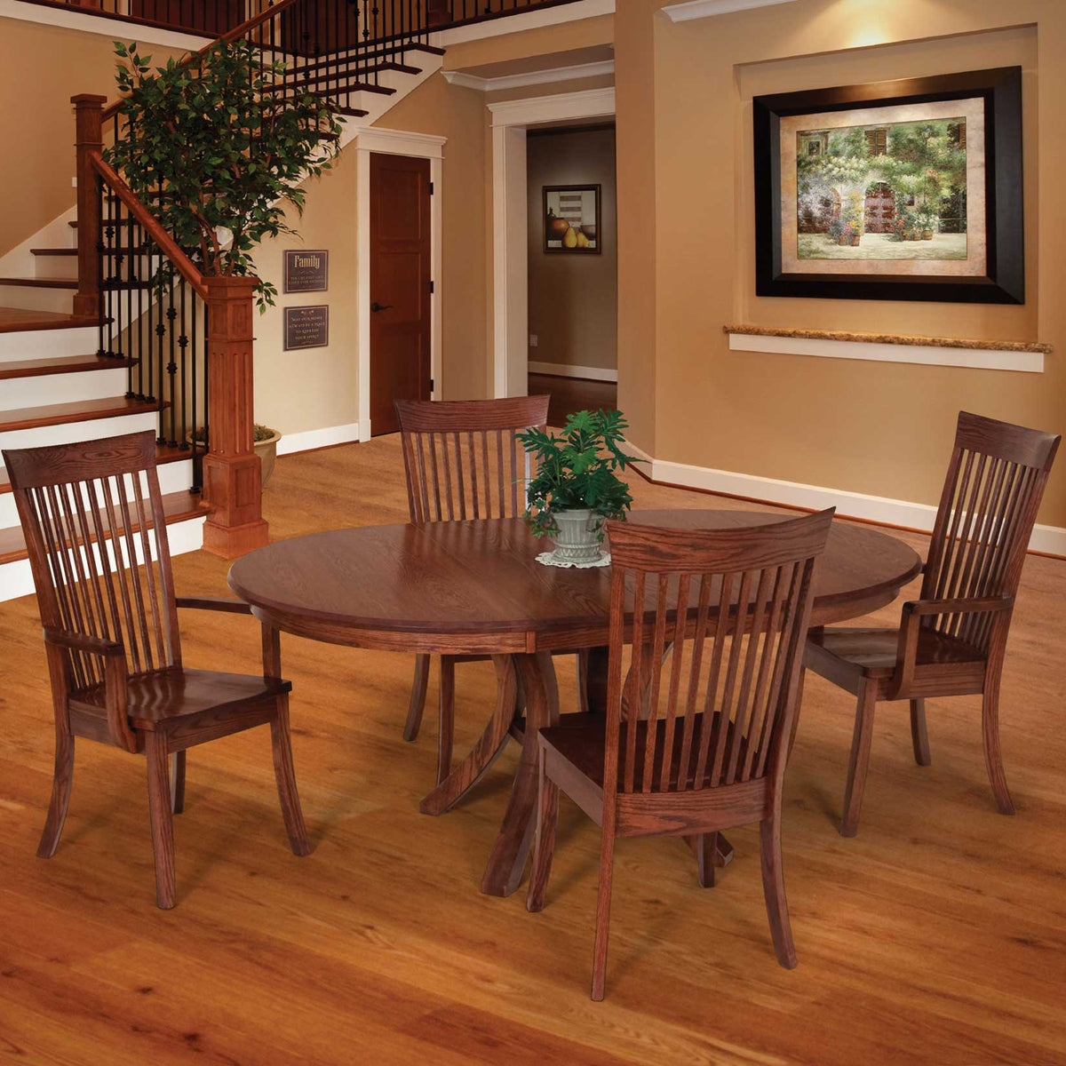 Round oak dining table with two slat back side chairs and two arm chairs beside a staircase in a warm entry