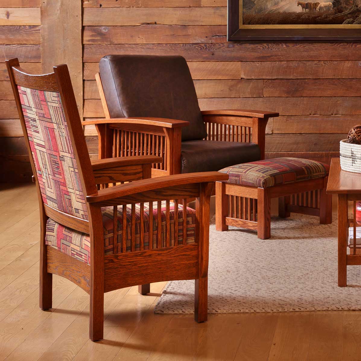 Two library chairs in red geometric upholstery with a leather Morris chair and ottoman in a log walled room