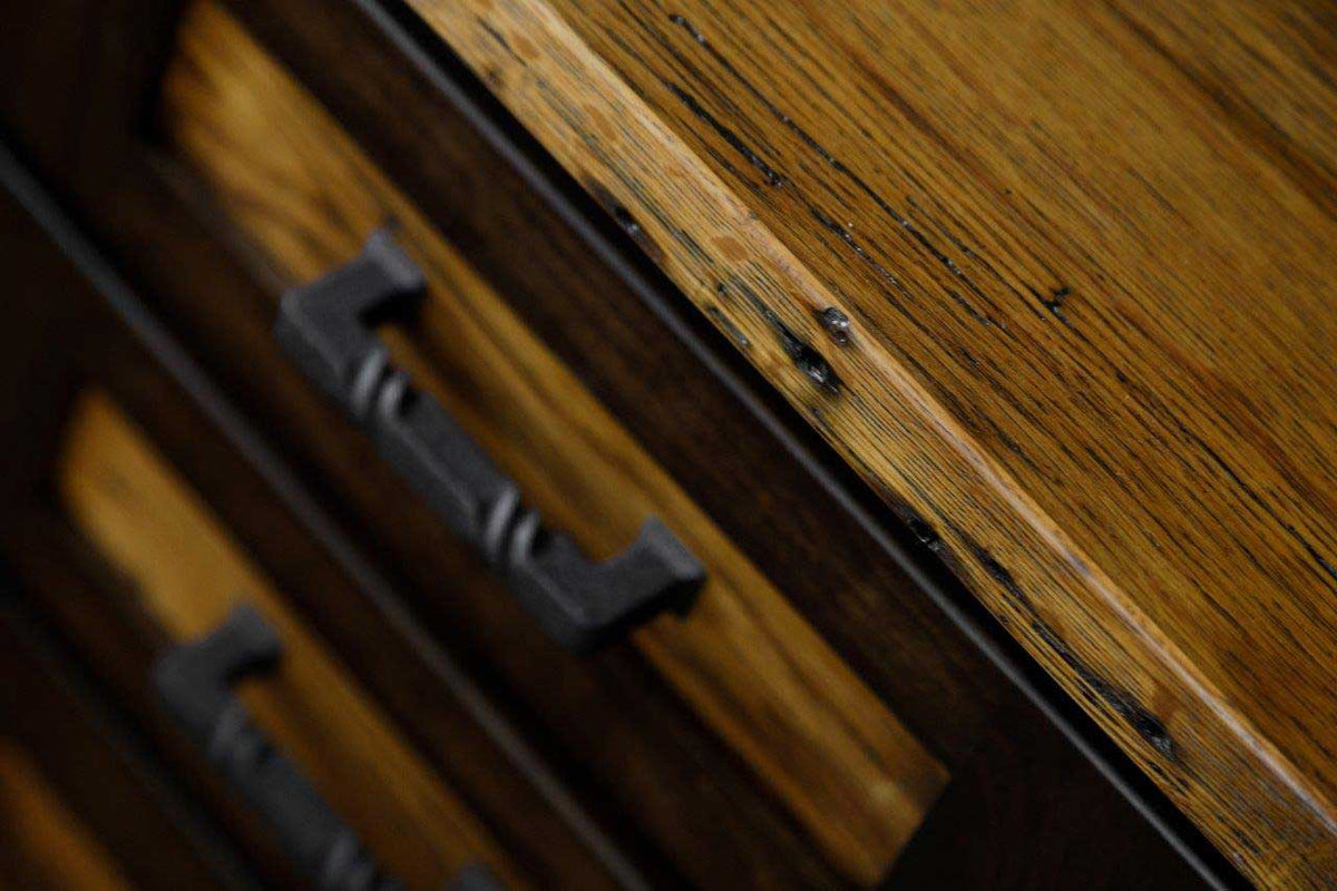 Row of black iron pulls receding along the reclaimed oak drawer fronts beneath the plank desk top