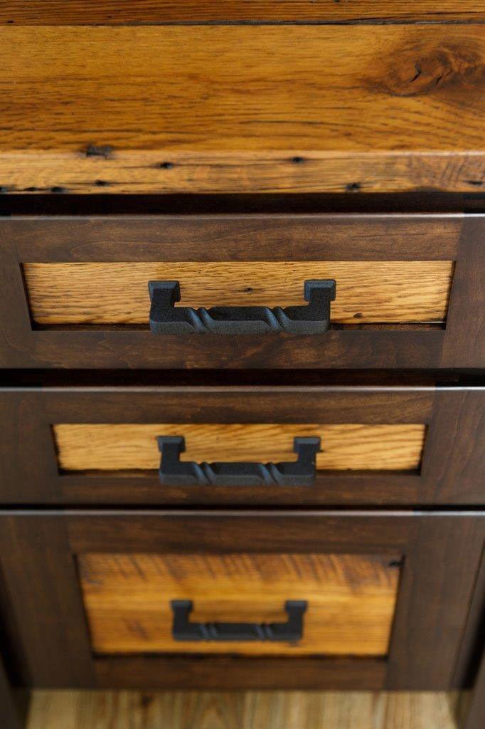 Detail of light oak drawer panels framed in dark wood with sturdy black bin pulls on the rustic desk