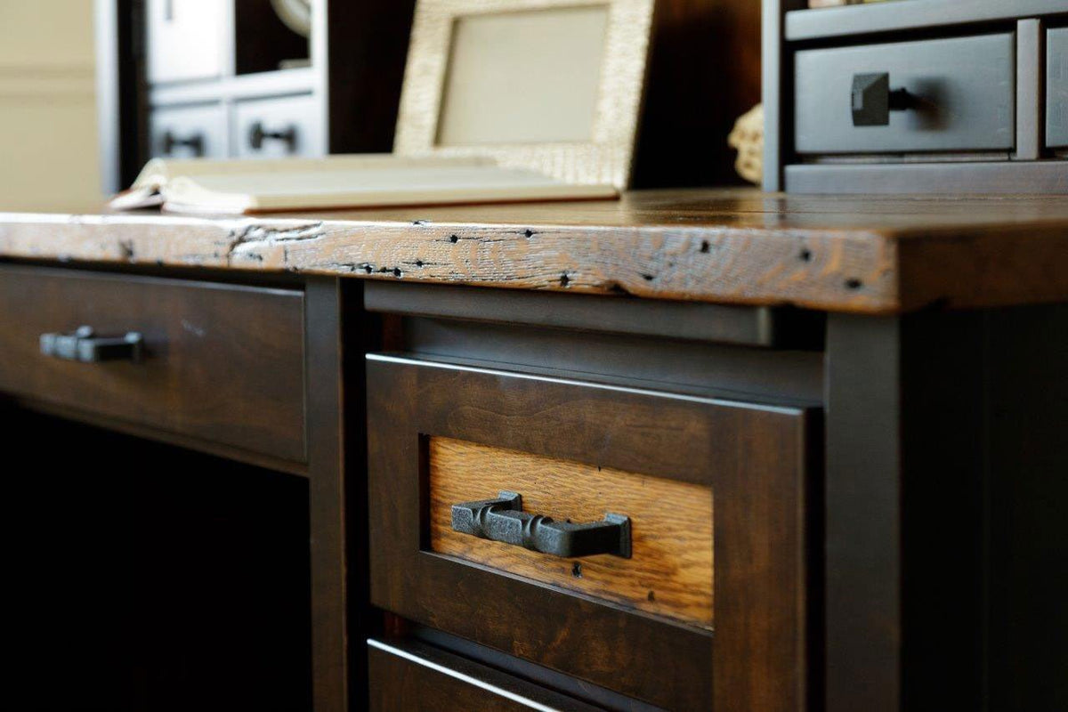 Live rough edge of the plank desk top over the dark pedestal, with a forged pull and framed picture behind