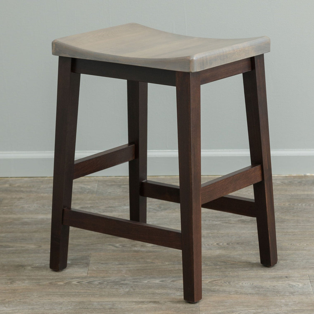 Bar stool with a weathered gray scooped saddle seat on a dark stained base with double side stretchers