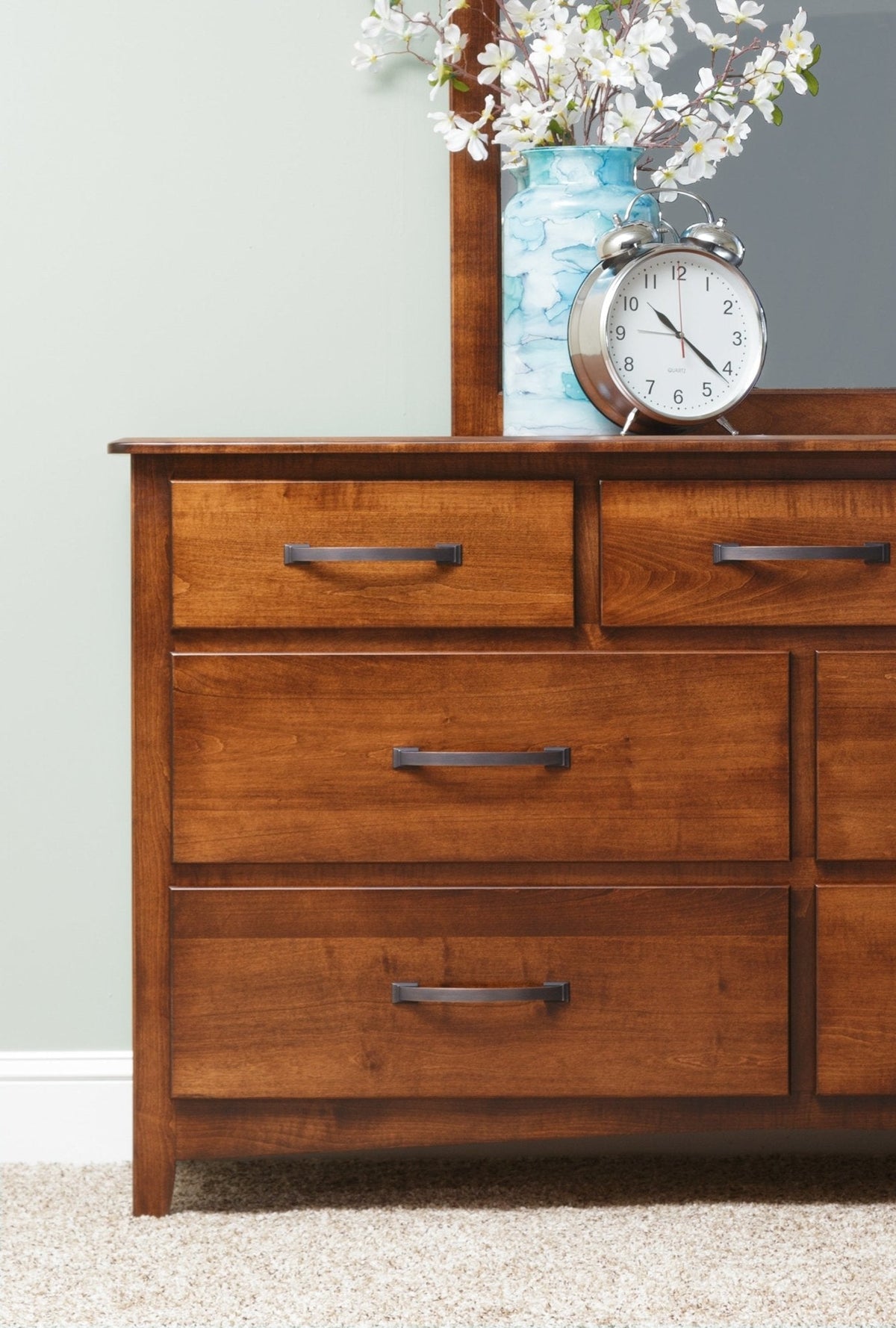Close-up of the brown maple dresser drawers and black bar pulls with the mirror frame and clock above