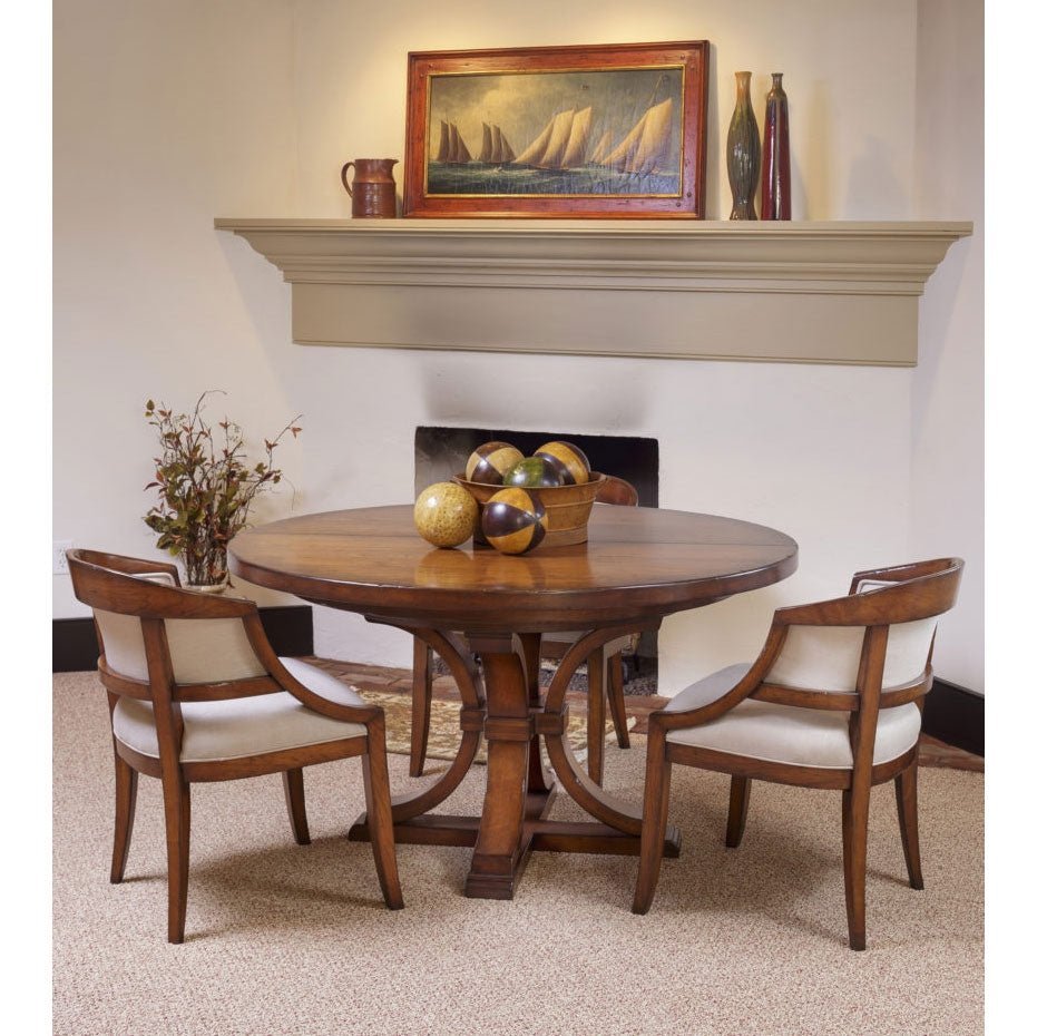 Cherry round dining table styled with decorative spheres and two cream upholstered chairs by a mantel