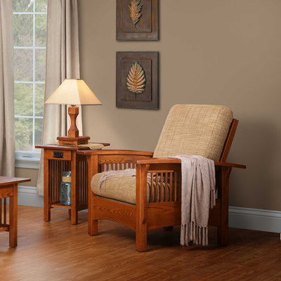Oak mission Morris chair with oatmeal cushions and a throw, beside a slatted end table and lamp by a window