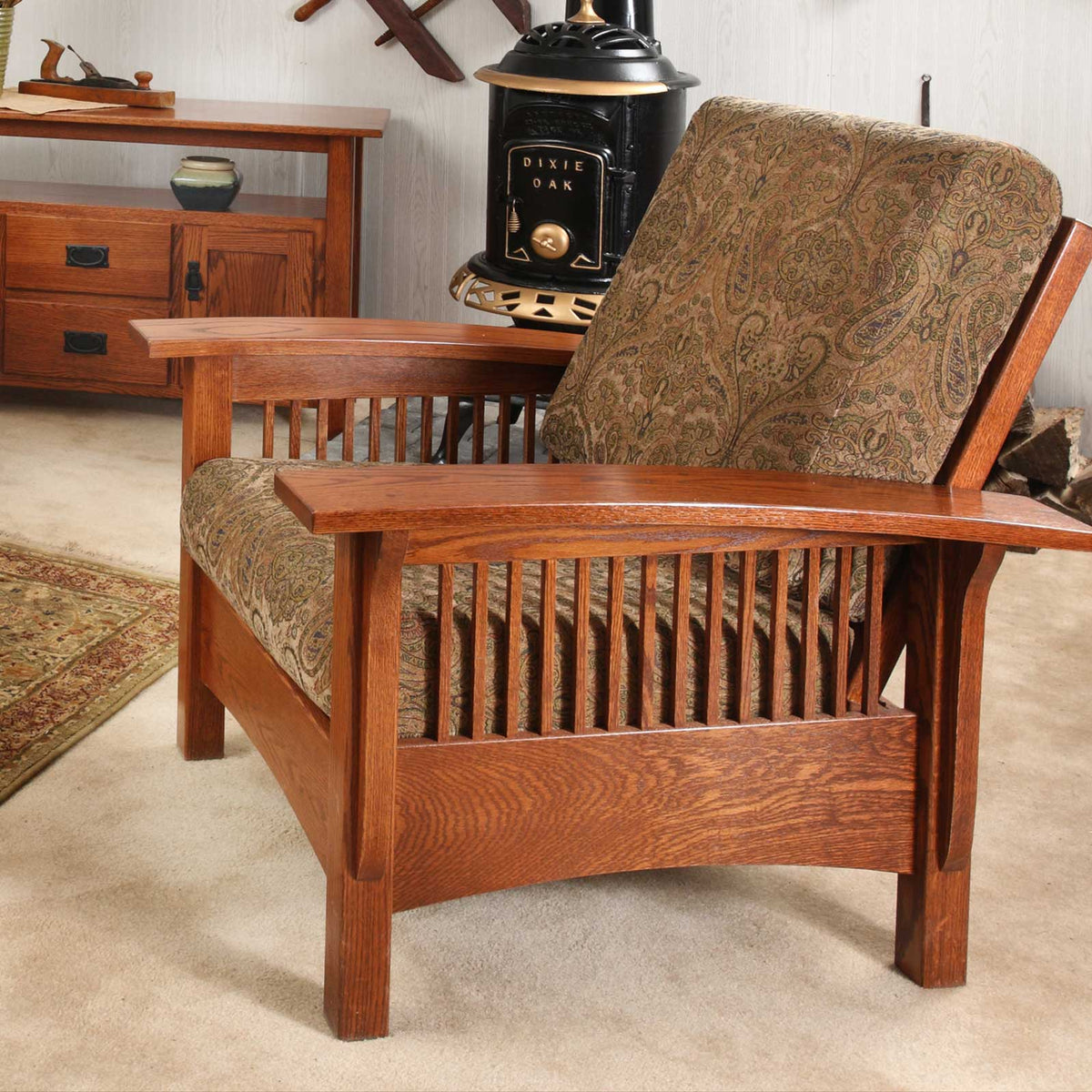 Quartersawn oak Morris chair with paisley cushions and spindle sides beside a vintage cast iron stove