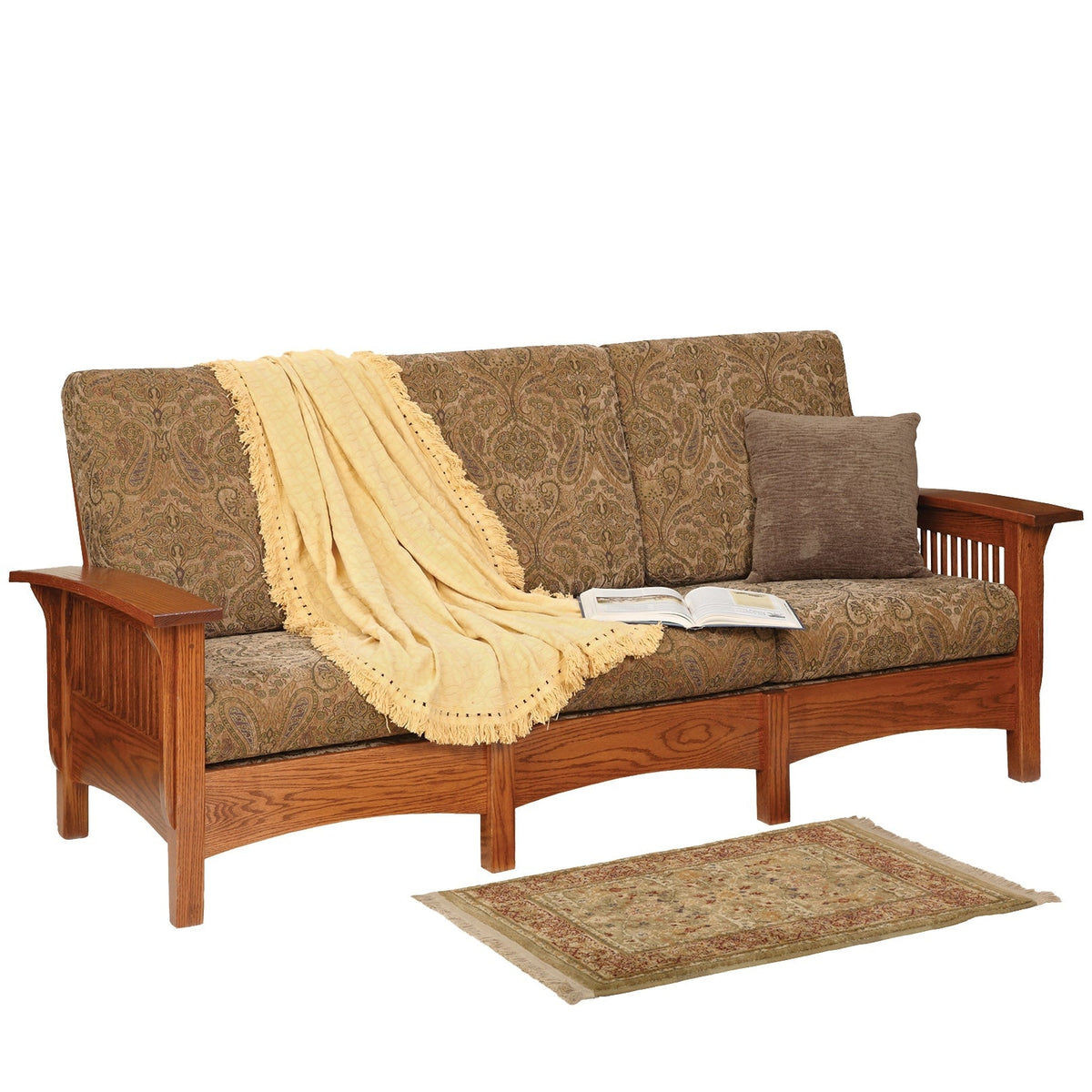 Oak mission sofa in olive paisley fabric with a cream fringed throw, book and pillow, beside a small rug