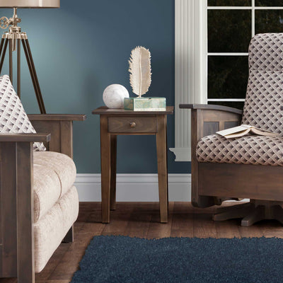 Gray stained shaker end table with one drawer and tapered legs between two upholstered chairs by a window