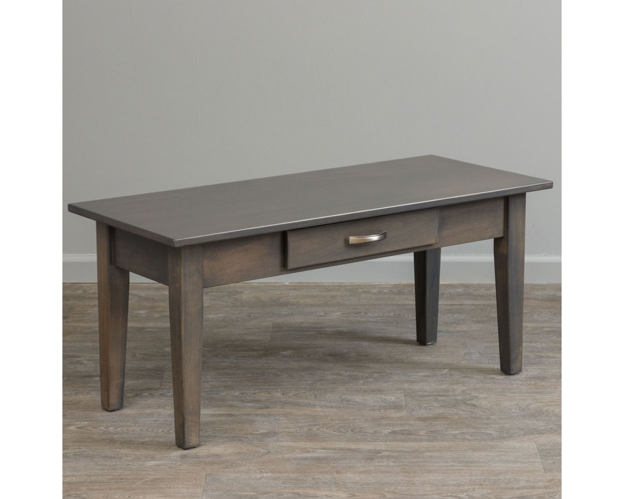 Gray stained Shaker coffee table with a center drawer, brushed nickel bar pull and tapered legs on light wood flooring