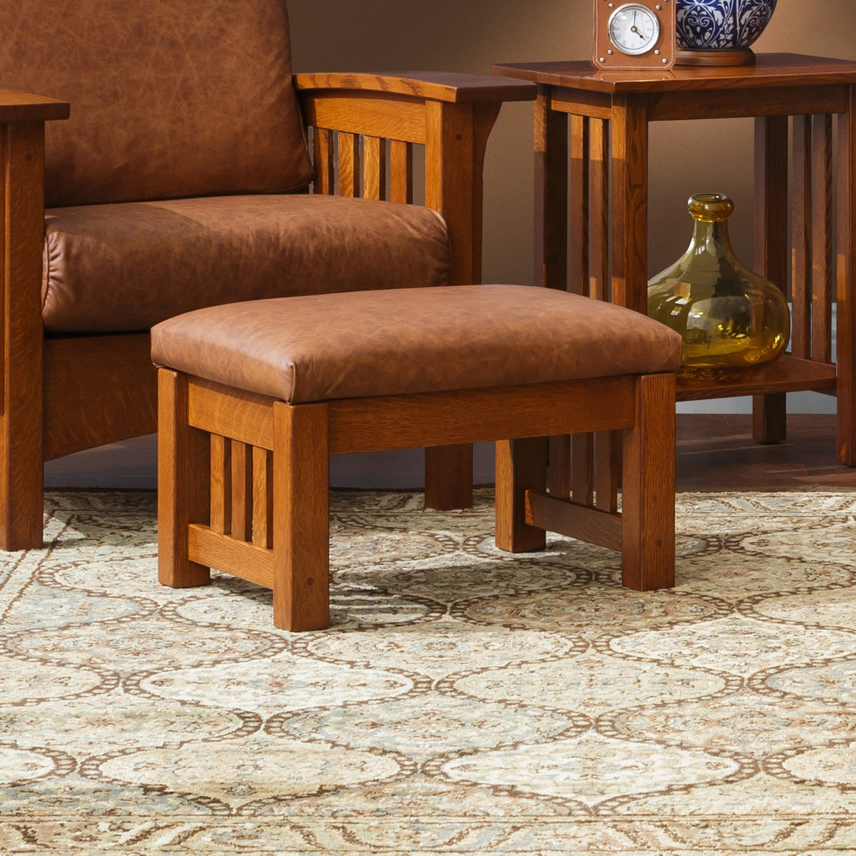 Quartersawn oak ottoman with distressed tan leather top styled on a patterned rug beside a matching leather chair