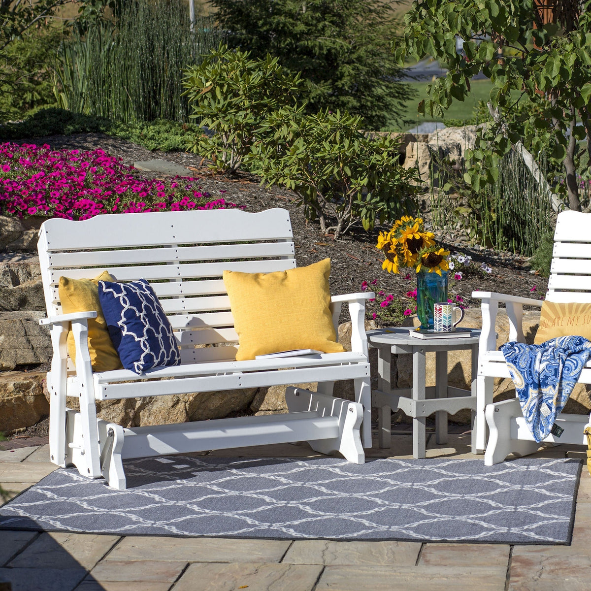 White poly glider bench with yellow and navy pillows beside a matching glider chair and side table