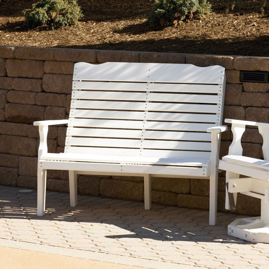 White poly curved back 4 foot patio bench with horizontal slats and contoured arms on a paver patio by a stone wall