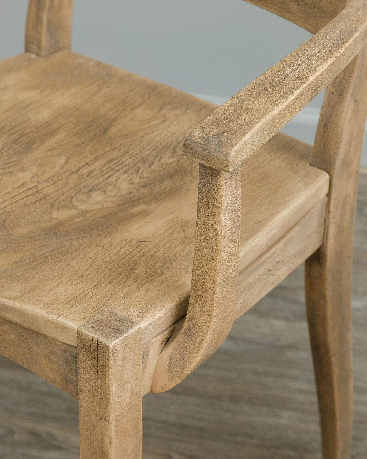 Detail of a rustic dining arm chair showing the curved arm, seat edge and hand distressed wood surface