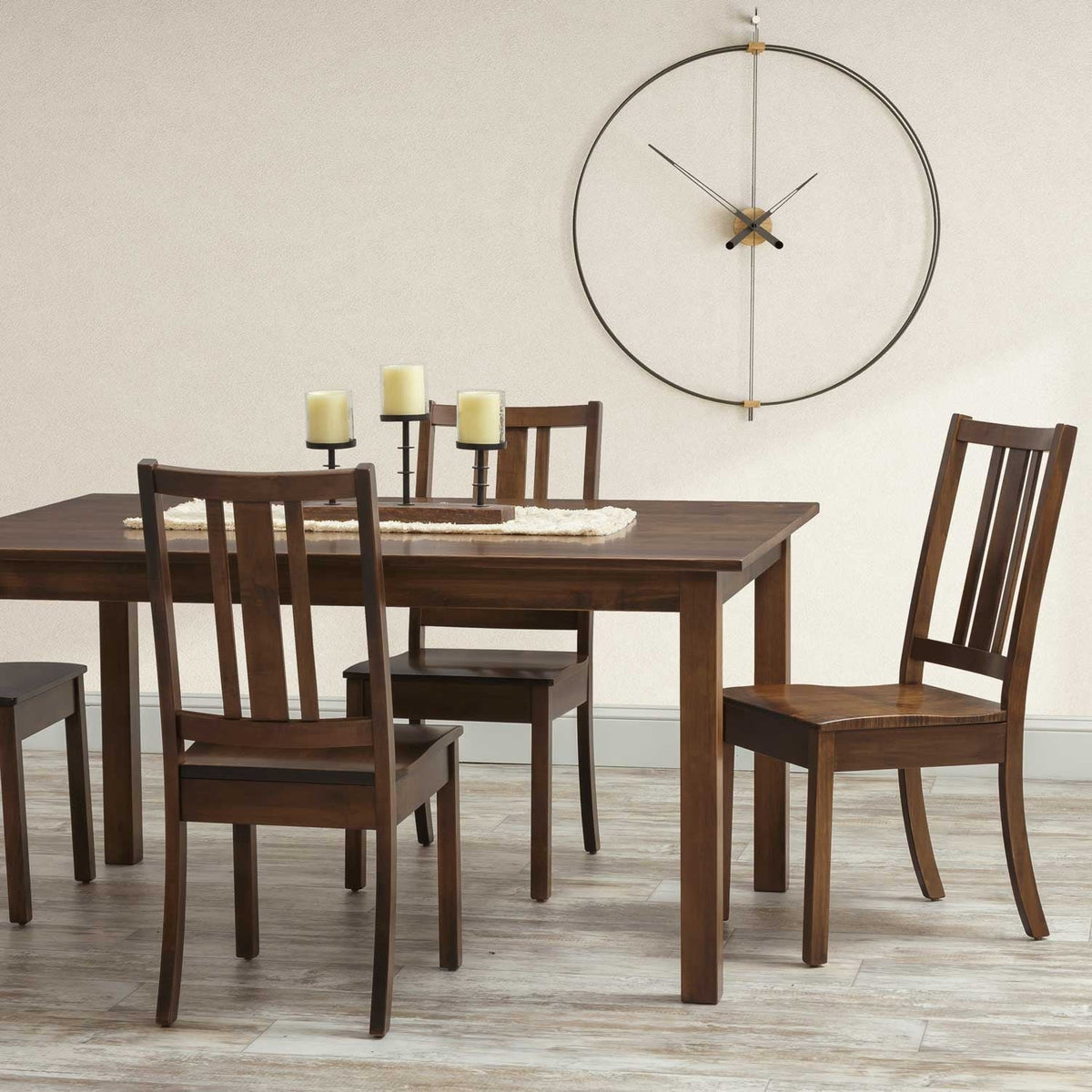 Rustic brown leg dining table with four slat back chairs, candles and a large ring wall clock behind
