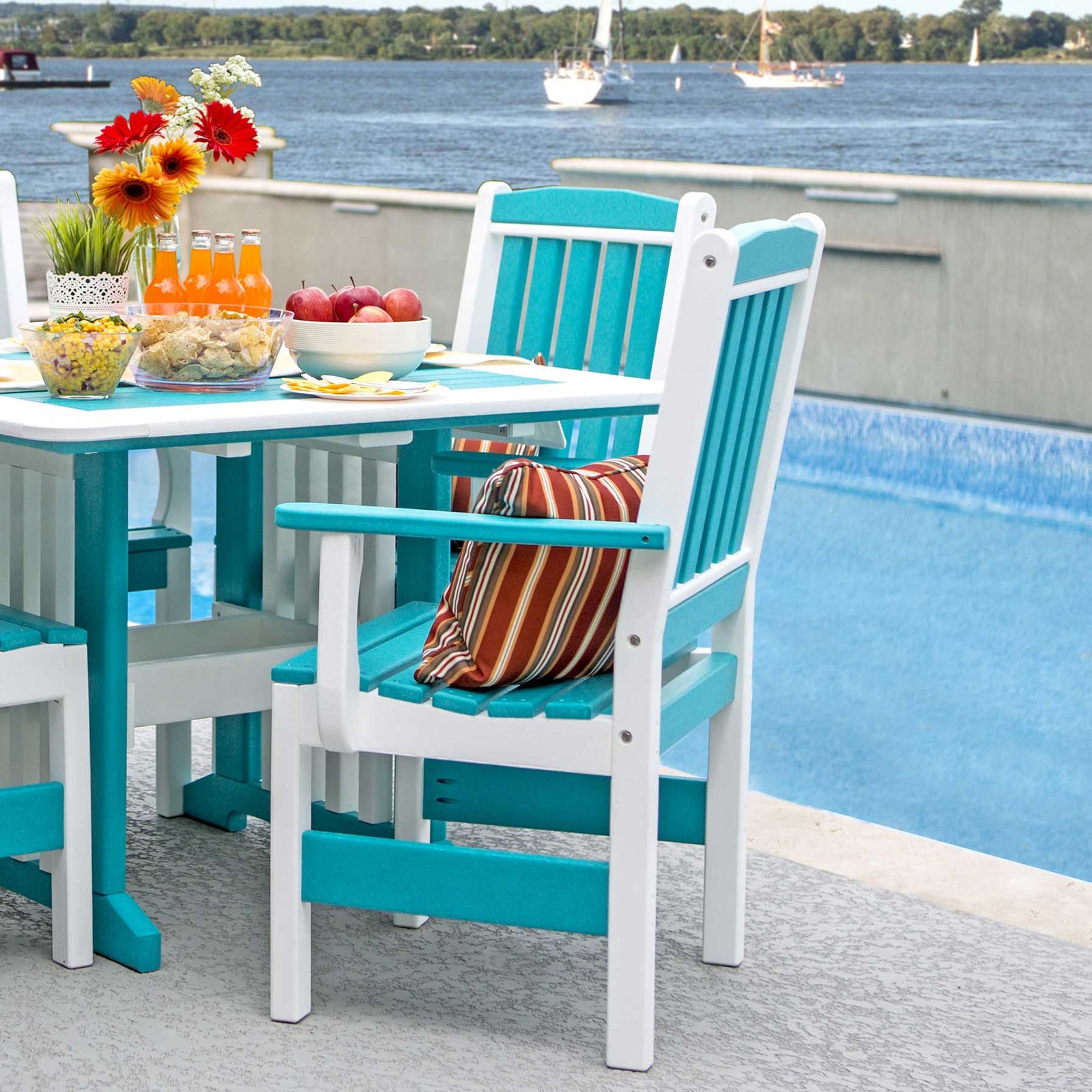 Aruba blue and white poly English Garden dining arm chairs at a patio table set with food by a pool overlooking the water