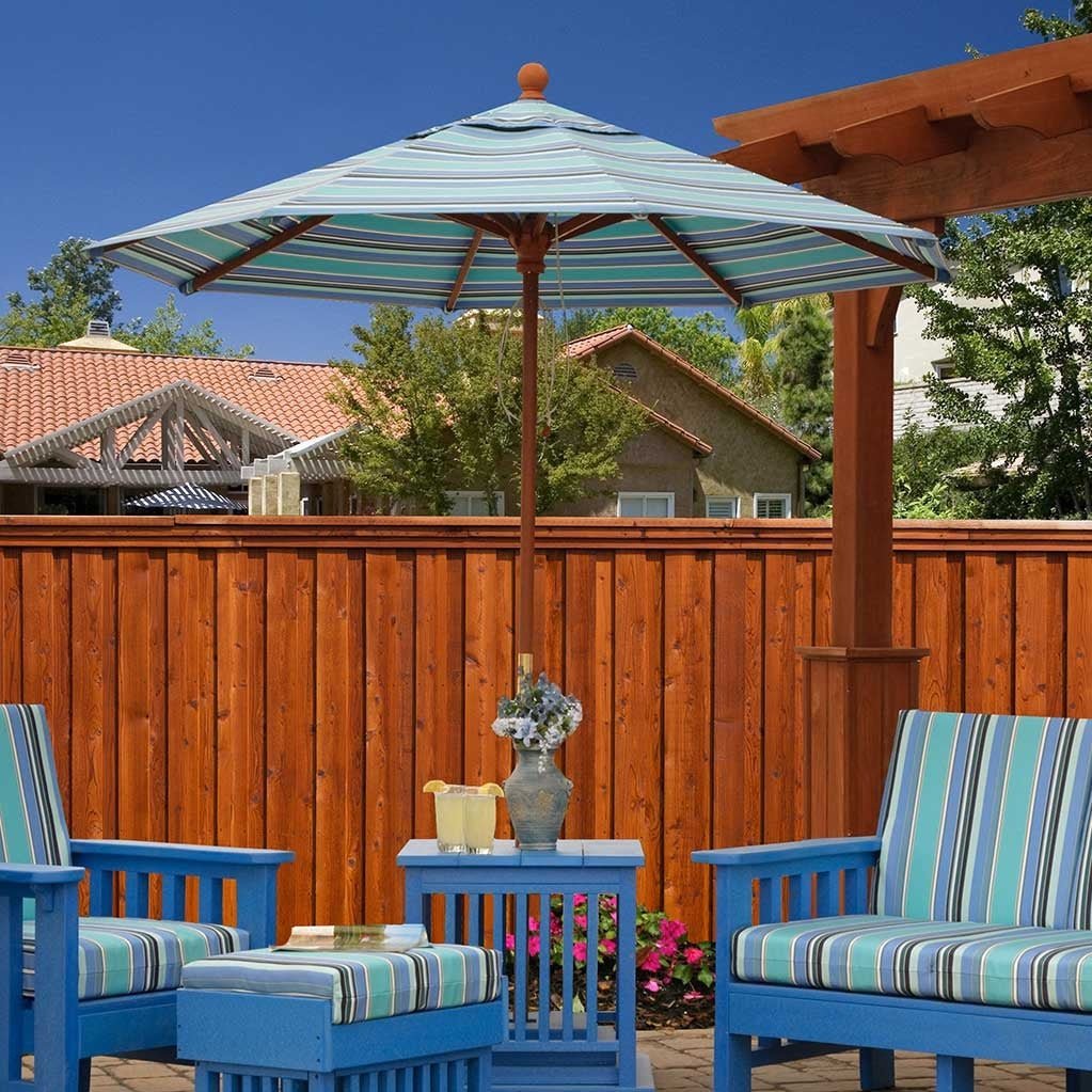 Blue and green striped umbrella with a woodgrain pole above blue poly Mission chairs and ottoman on a patio