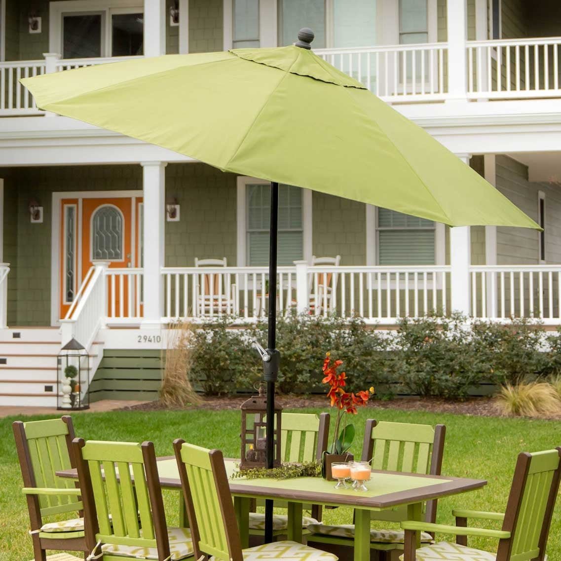 Green canopy umbrella shading a brown poly dining table with green slat back chairs beside a porch
