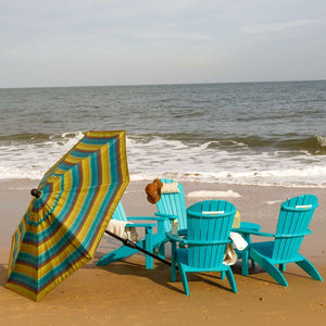 Tilted teal and gold striped umbrella beside turquoise poly Adirondack chairs on a sandy beach