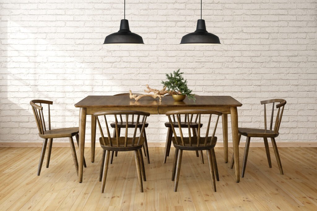 Mid century walnut dining table with six curved spindle chairs under black pendant lights by a brick wall