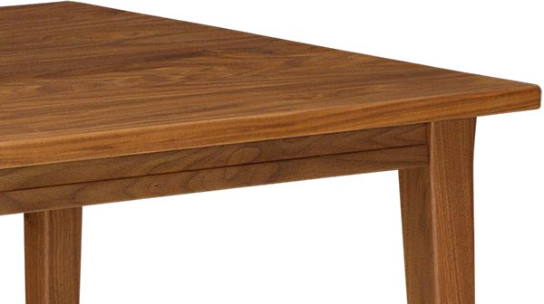 Detail of a walnut dining table corner highlighting the smooth grain, rounded edge and apron