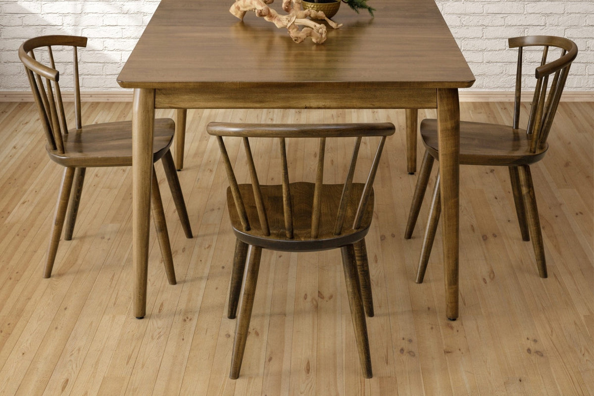 Walnut dining table with three curved spindle back chairs on a pine floor against a white brick wall