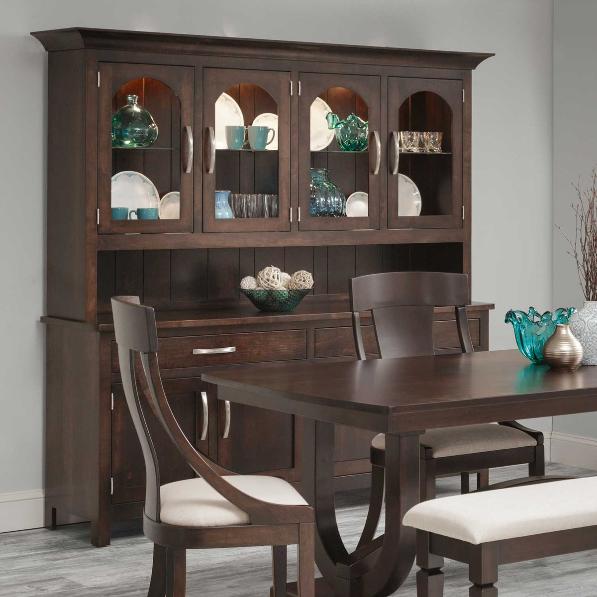 Espresso four-door china hutch filled with teal glassware above an open server, with matching dining chairs