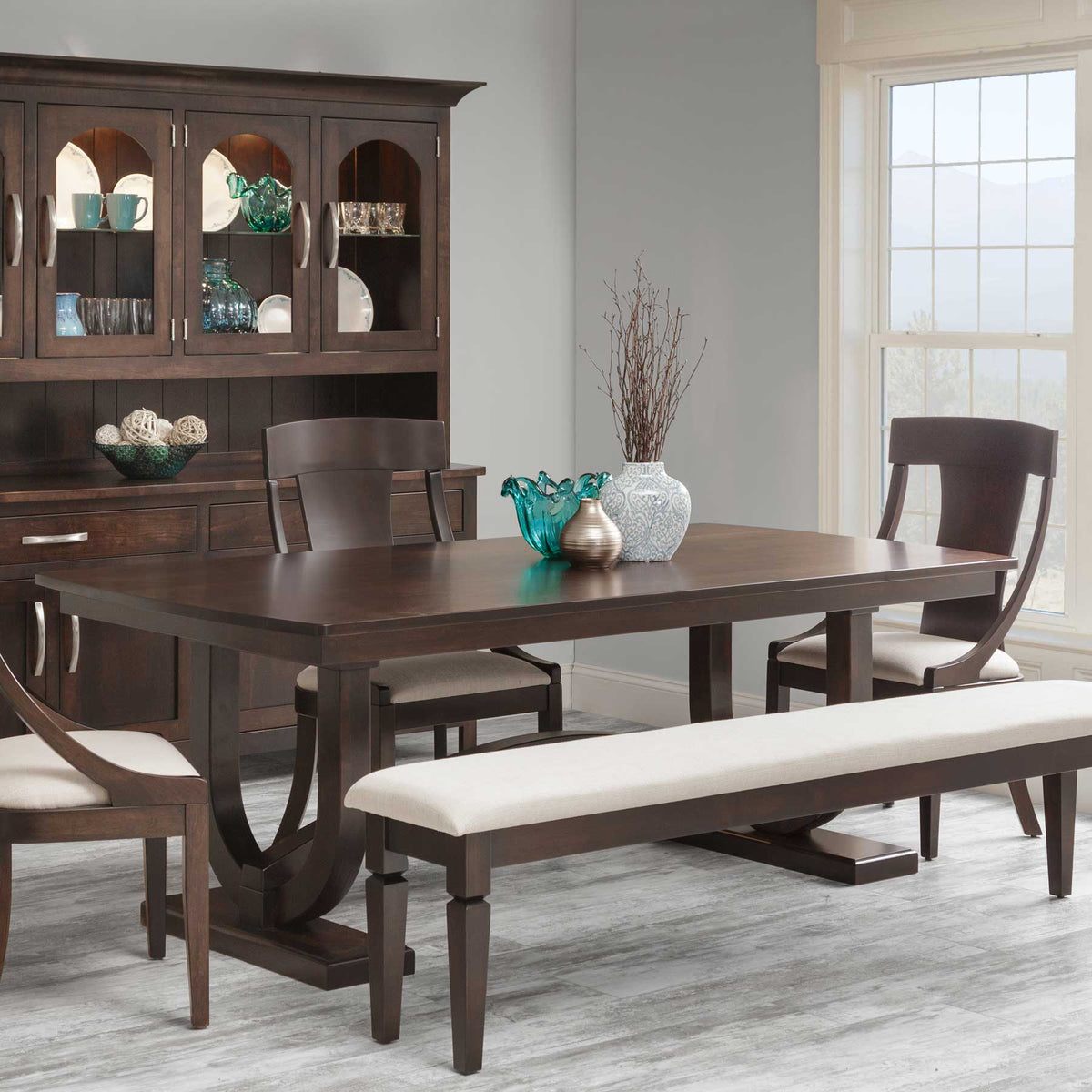 Dark brown trestle dining table set with three wood-back chairs, cream bench and a matching lighted china cabinet behind