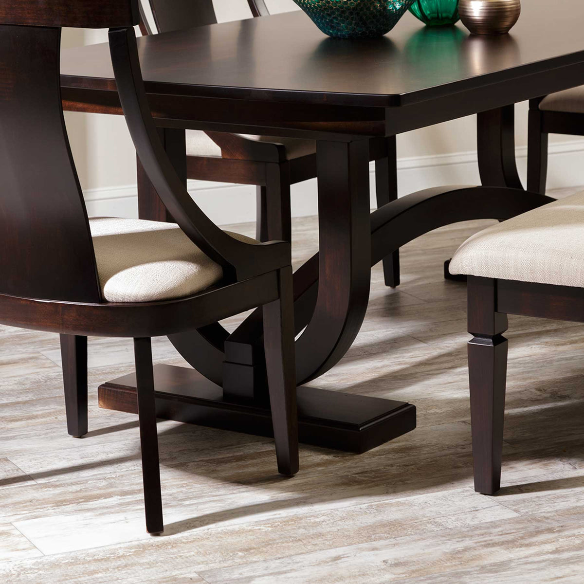 Close-up of the trestle table's curved arch pedestal base and beveled plank foot beside a chair and cream upholstered bench