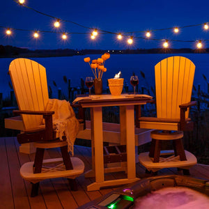 Two swivel Adirondack bar chairs and a square poly table set with wine under string lights beside a lake and hot tub