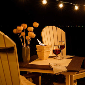 Close up of the square poly bar table at night with wine glasses, napkins and a lit fire pot between chairs