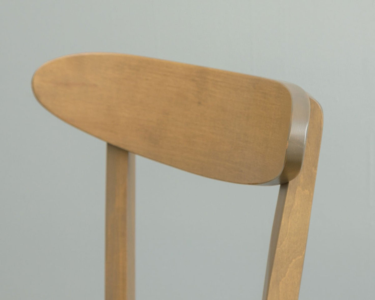 Close-up of the light stained chair's rounded oval back panel joined to the curved rear post against a gray wall