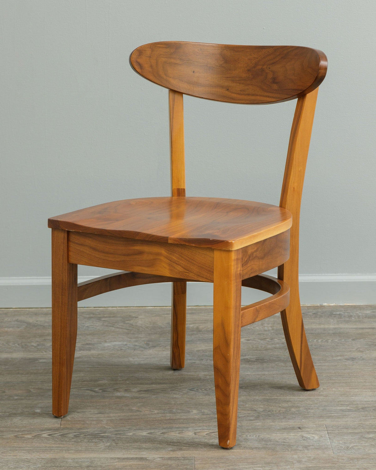 Mid century modern dining chair in natural walnut with an oval floating back rest, saddle seat and splayed tapered legs